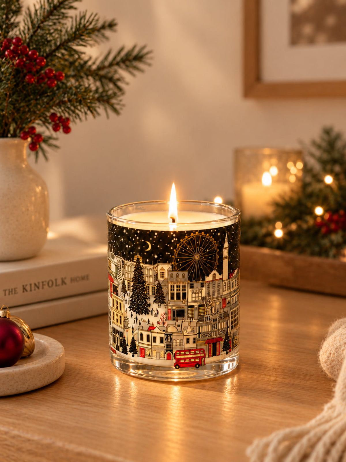 A scented candle  decorated with a festive Christmas London cityscape illustration featuring red double-decker buses,  and snow-covered landmark buildings and attractions